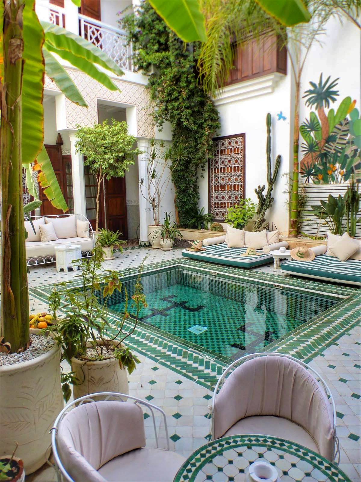 Patio de riad marrakchi avec bassin en zellige vert, bananiers et salons bas